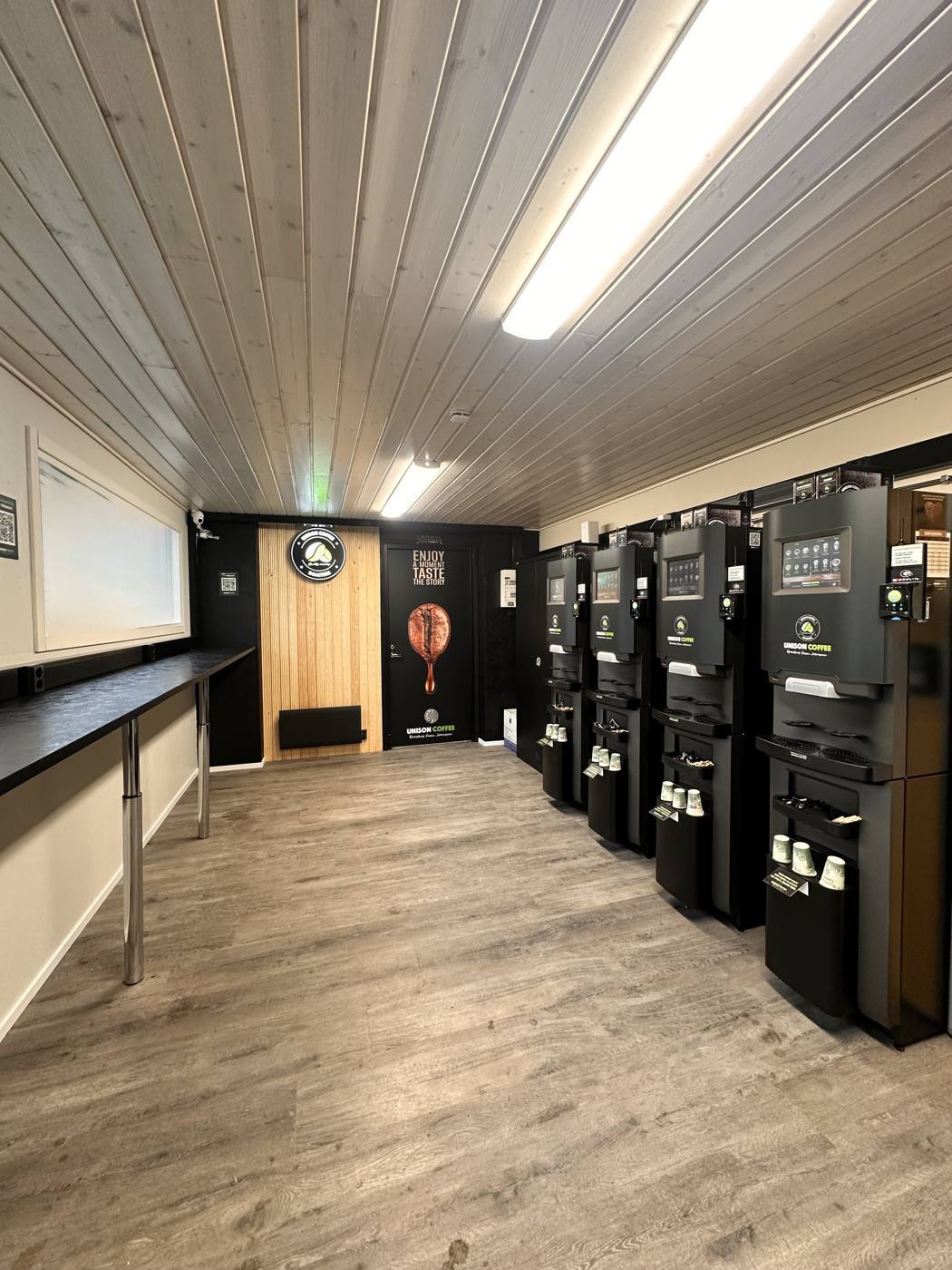 Kahvikontin sisätila ikkunoiden puolelta: kahvikoneet, älyjääkaappi ja vaalea lattia